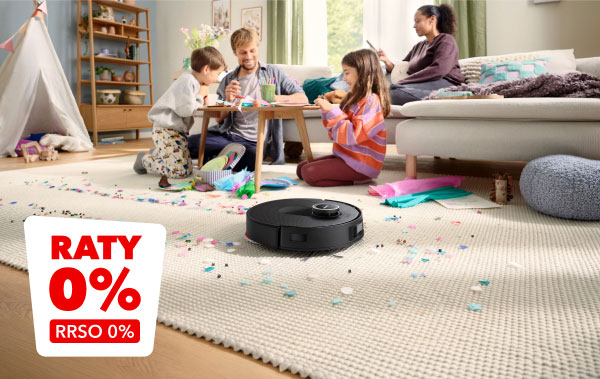 Na zdjęciu widać salon z jasnym dywanem, na którym leży robot sprzątający otoczony kolorowymi papierkami. W lewym dolnym rogu znajduje się czerwony napis RATY 0% RRSO 0%.