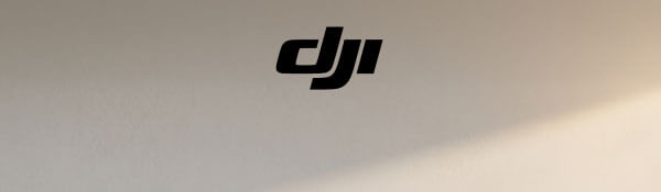 Czarne logo dji umieszczone jest na jasnym tle z delikatnym cieniowaniem. Tło przechodzi z szarości w jaśniejszy odcień, tworząc subtelny gradient.