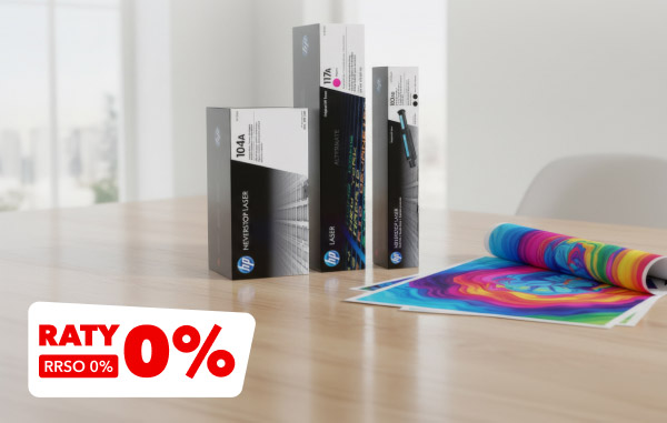Na drewnianym stole znajdują się pudełka z tonerami oraz rozwinięty, kolorowy wydruk. W lewym dolnym rogu widnieje czerwony napis RATY 0%, RRSO 0%.